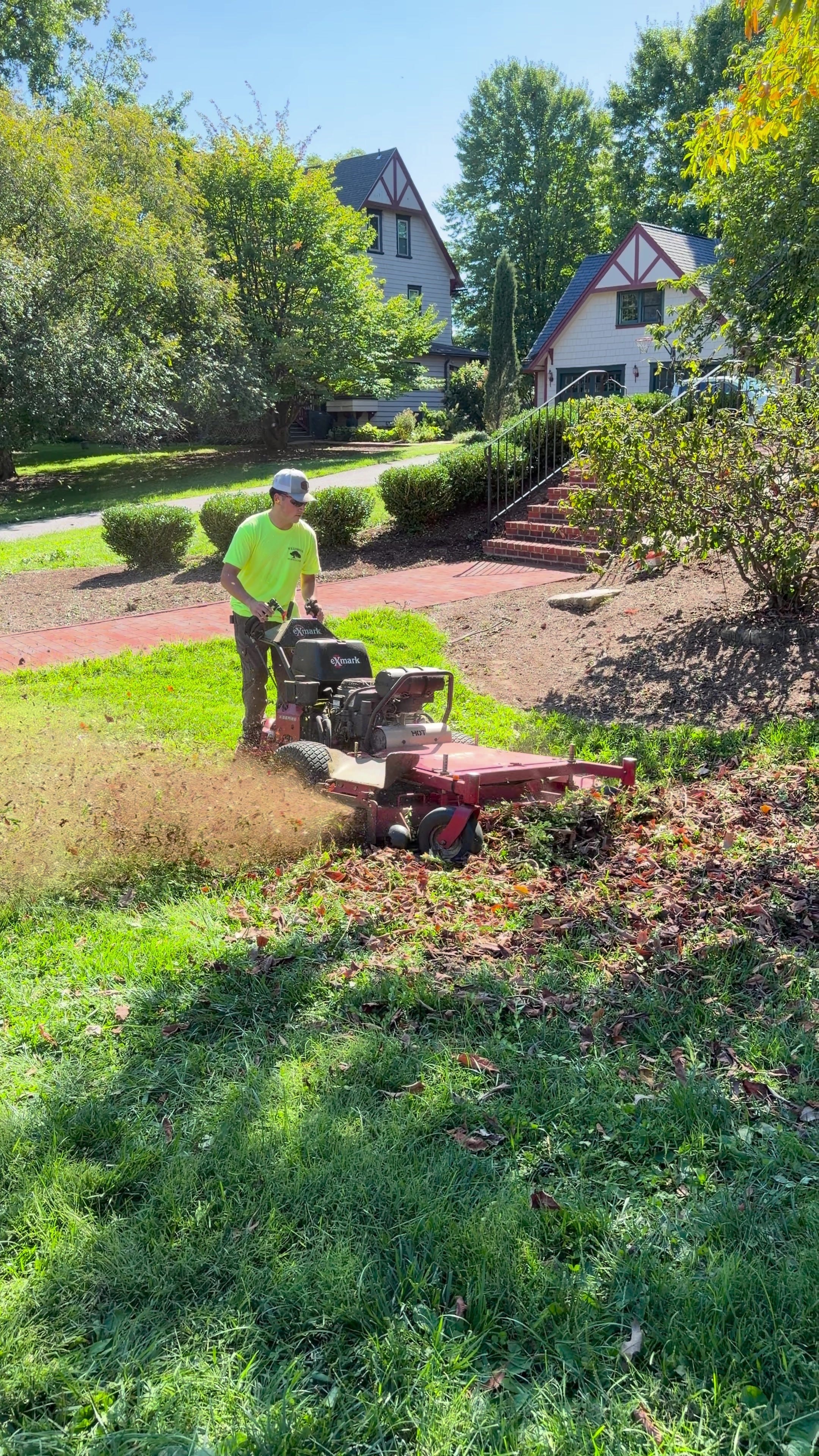 A Dragan Landscaping crew member mowing a lawn beside a brick walkway